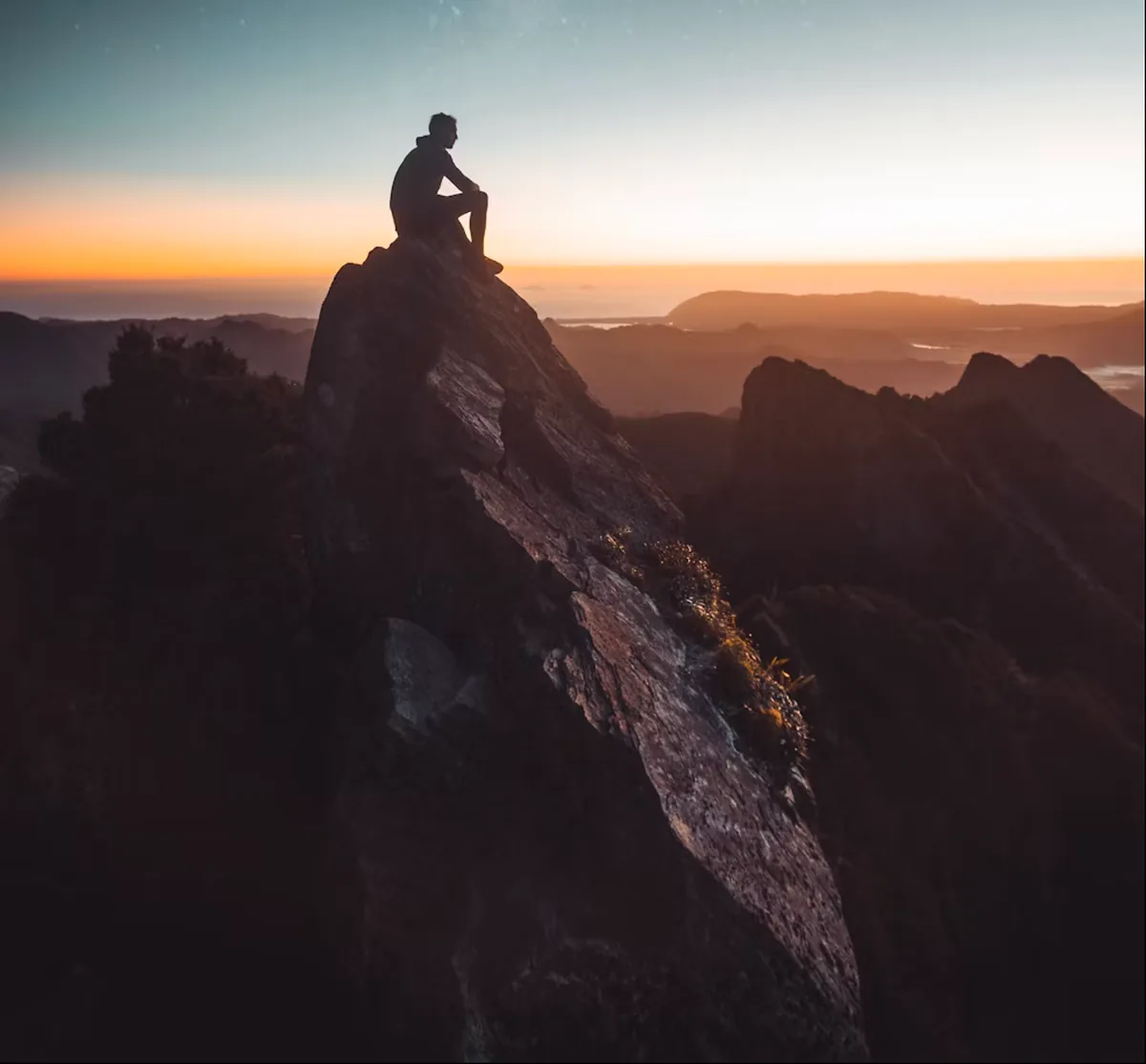 A lone figure sitting on a rocky summit above the clouds at sunrise