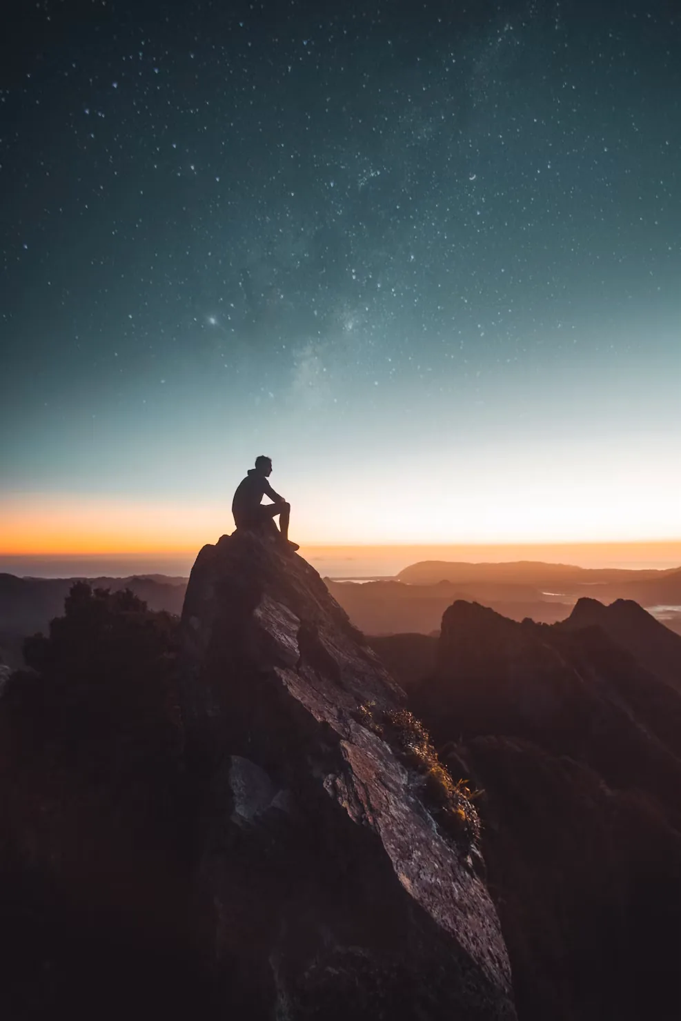 A lone figure sitting on a rocky summit above the clouds at sunrise